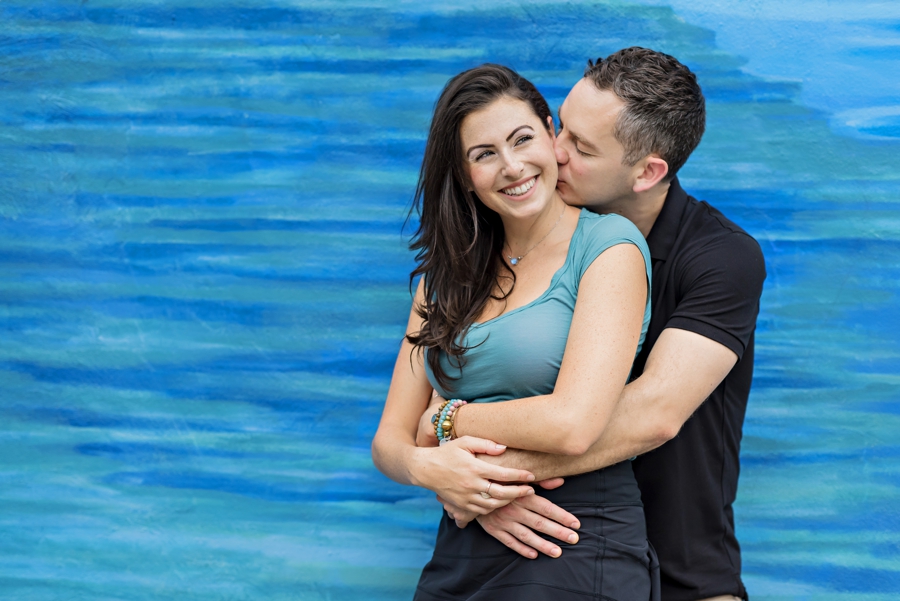 A man kisses his fiance in front of a blew wall.